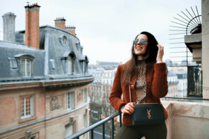 Une jeune femme à la mode prend la pose sur un balcon parisien pendant un week end shopping à Paris.